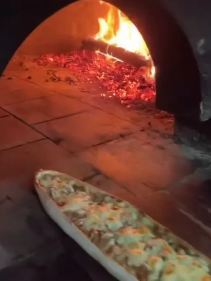Odun fırınının ağzında, kürekte pişmeye giden kıymalı pide